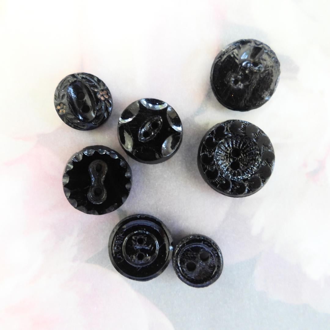 Set of 7 antique Victorian black glass buttons for sewing - 2-hole, 8–15 mm, Czech molded glass. Glossy floral & geometric patterns