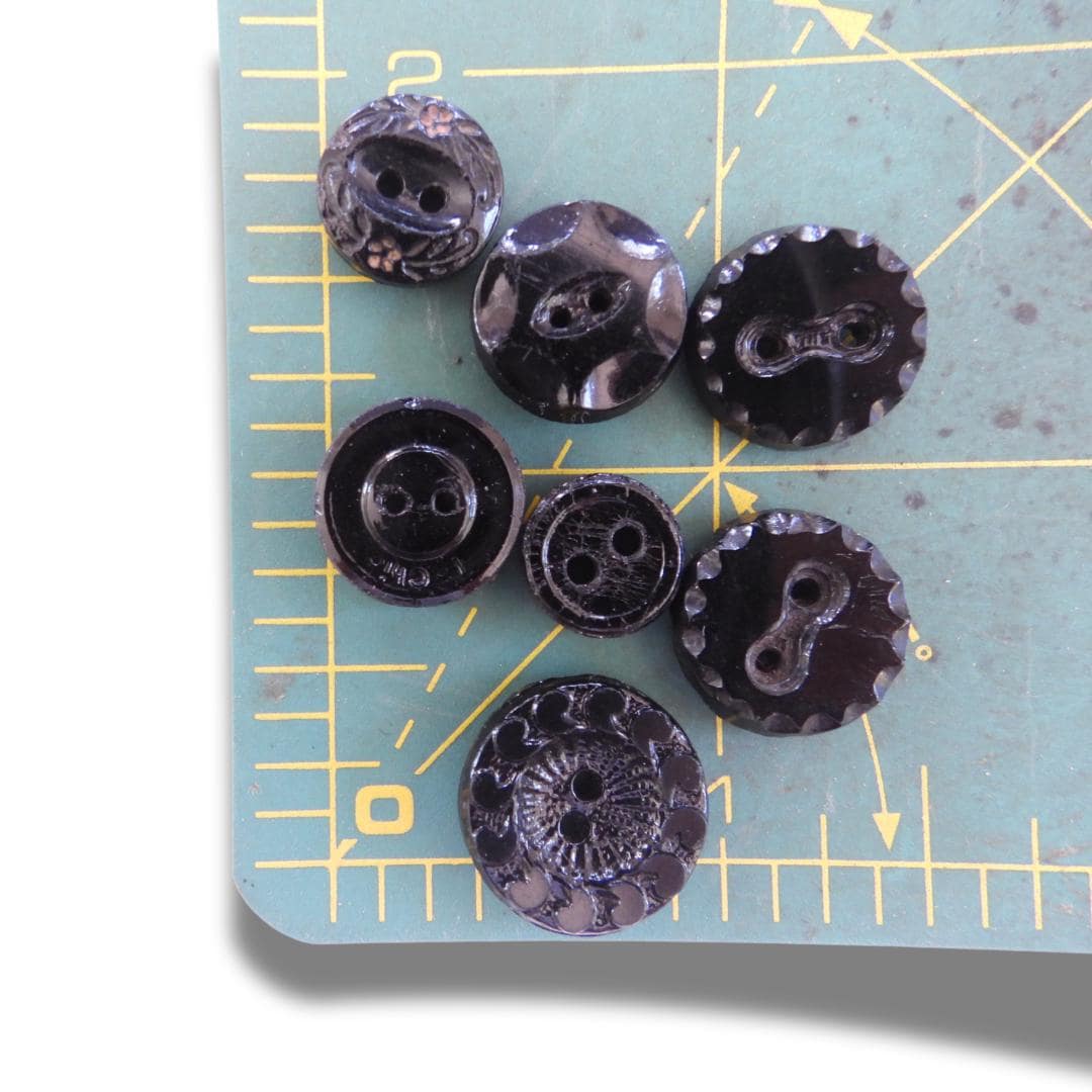 Set of 7 antique Victorian black glass buttons for sewing - 2-hole, 8–15 mm, Czech molded glass. Glossy floral & geometric patterns